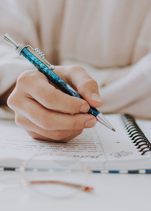 Close-up of a hand writing in a spiral notebook with a blue pen